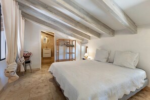 A bedroom with a large bed, a wooden ceiling, a bathroom with a mirror, and a window with curtains.