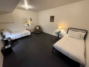 A room with two beds, a chair, a small table, and a wall-mounted mirror.