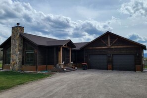 A two-story building with a stone chimney, large windows, and a gravel driveway.