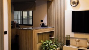 Un salon moderne comprenant un canapé, une table basse, un téléviseur et un coin cuisine visible à travers une porte ouverte.