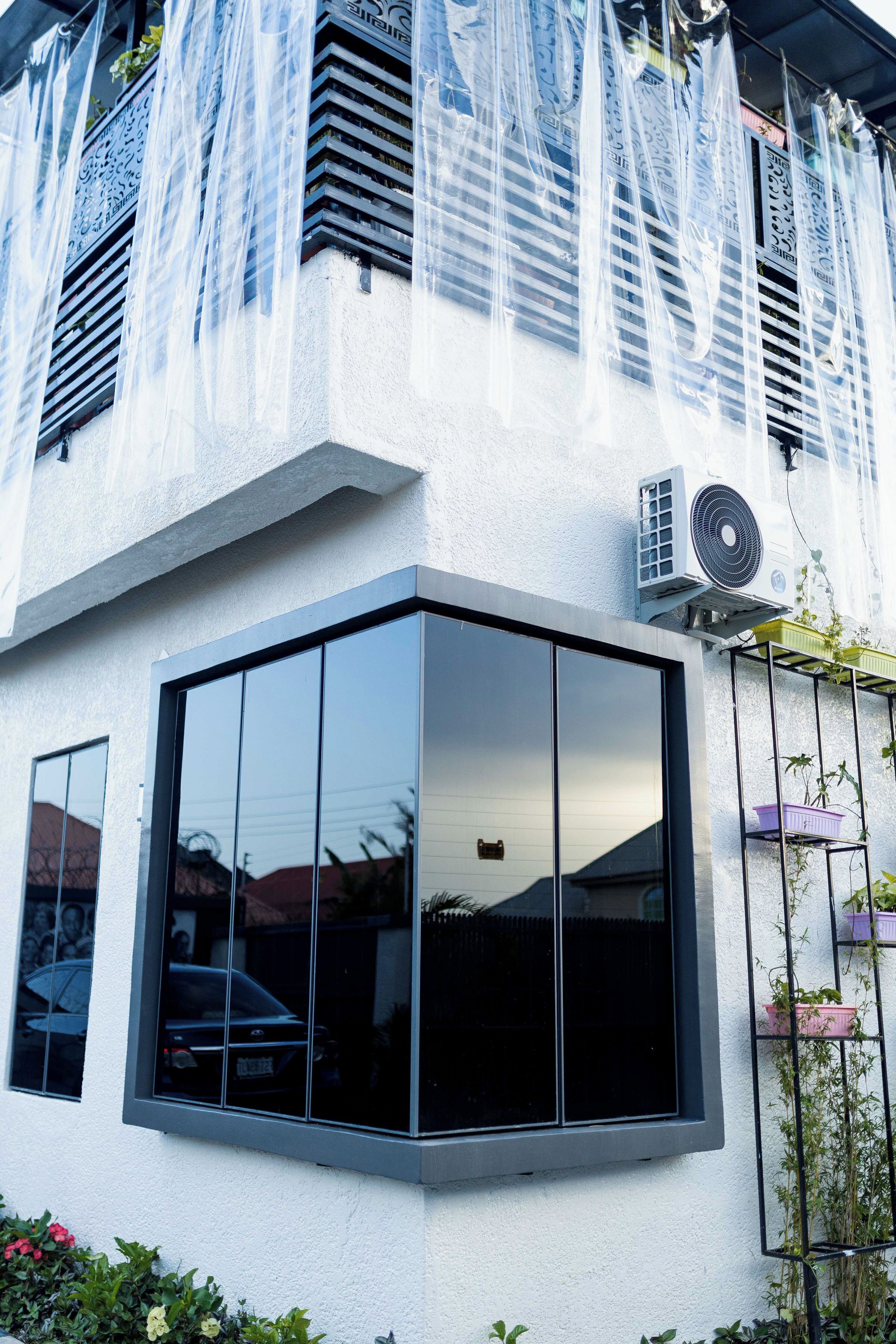 Um edifício com uma grande janela de vidro transparente, parede exterior branca e um aparelho de ar condicionado fixado na parede.