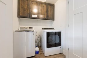 A laundry room with two white appliances, one dryer and one washer, under wooden cabinets. - Teewinot Townhome - Yellowstone, Targhee, Tetons (Victor)