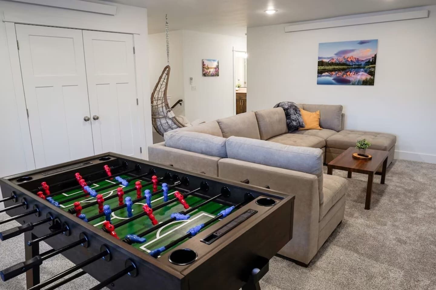 Un salon avec une table de baby-foot, un canapé, une table basse et un tableau accroché au mur.
