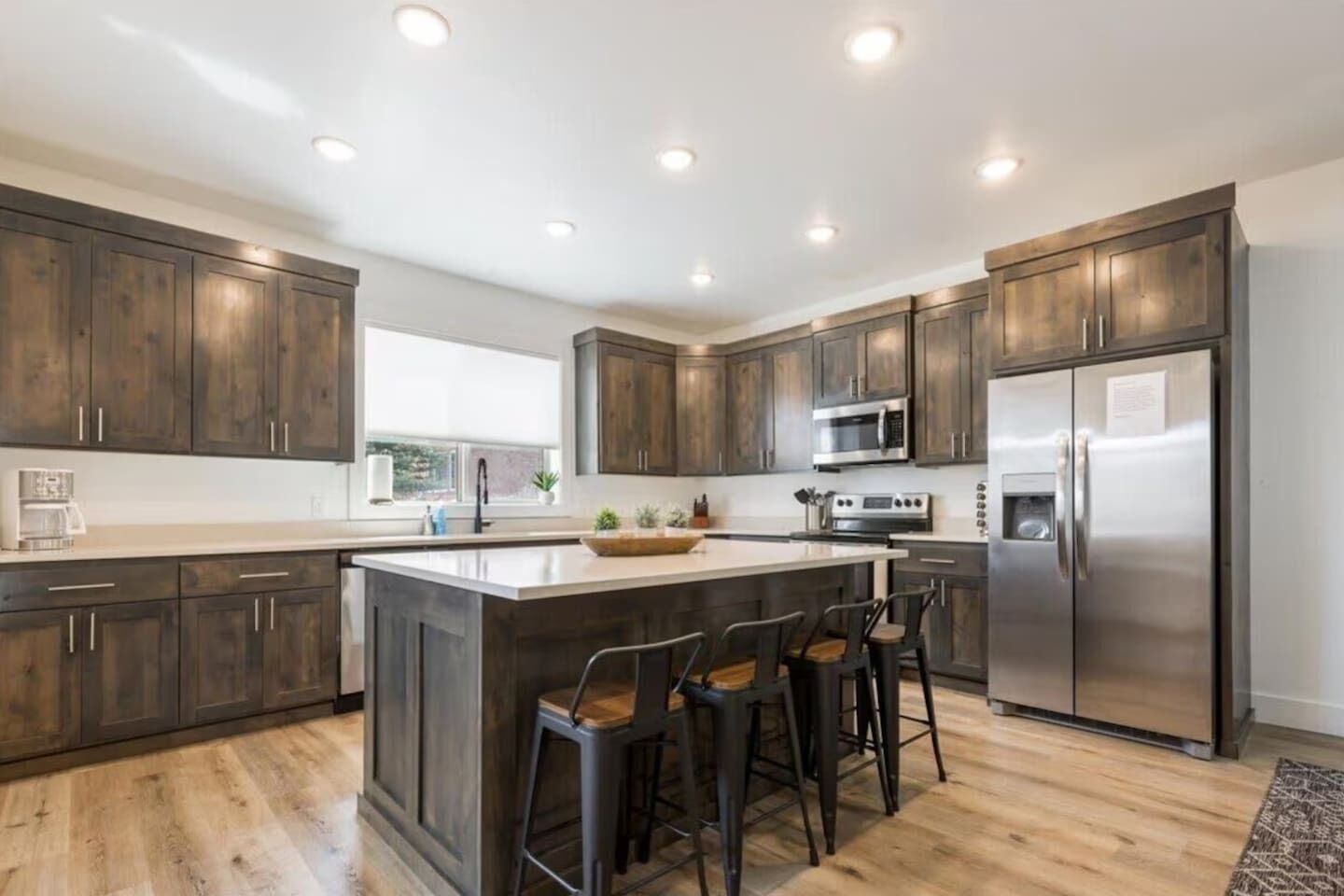 A modern kitchen with dark wood cabinets, stainless steel appliances, and a central island with bar stools.