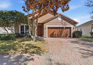 A residential house with a garage, a driveway, and a tree with autumn leaves. - Bridgeford Splash Retreat (Davenport)