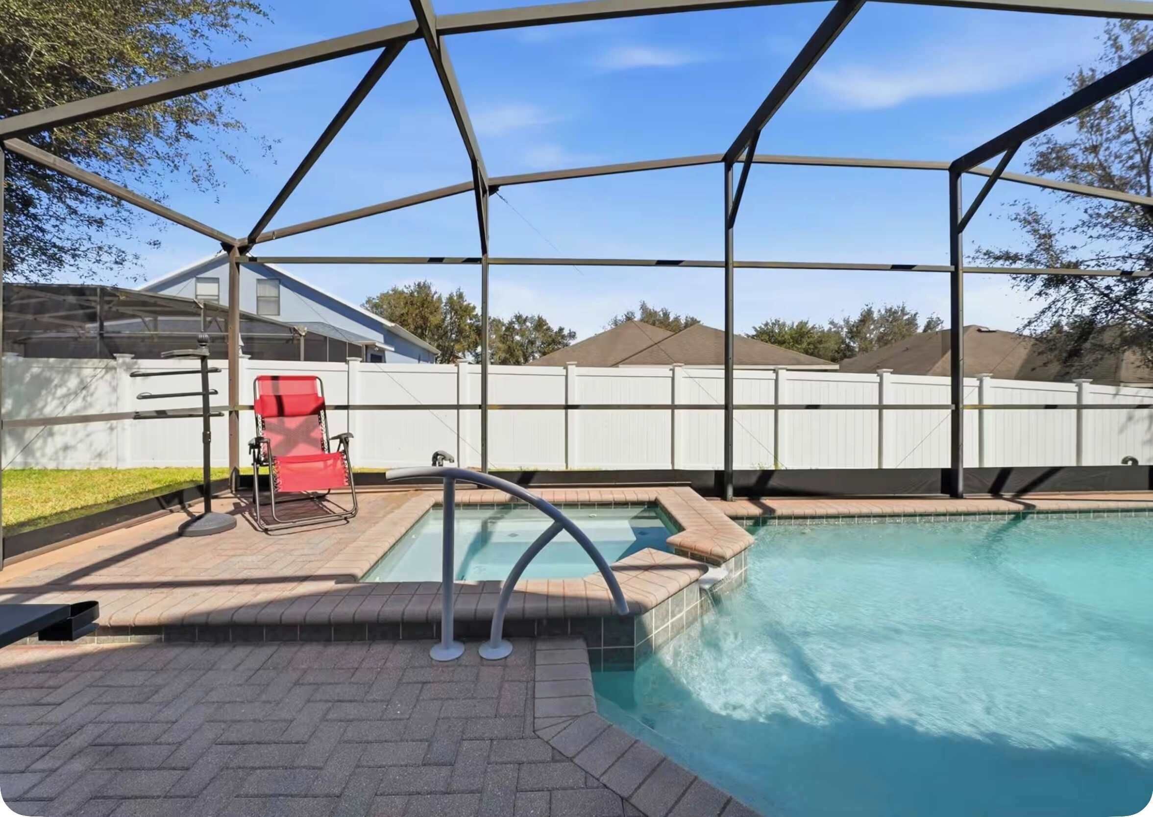 A swimming pool with a covered area, a red chair, and a white fence in the background.