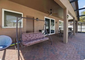 A covered patio area with a swing chair, a cushioned bench, and a dining table with chairs. - Bridgeford Splash Retreat (Davenport)