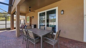 Eine Terrasse im Freien mit Tisch und Stühlen, einem Deckenventilator und einer Glastür, die zu einem überdachten Bereich führt.