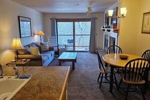 A living room with a sofa, a coffee table, a dining table with chairs, a fireplace, and a large window with curtains. - Quiet condo near Targhee, Yellowstone, and Tetons. (Driggs)