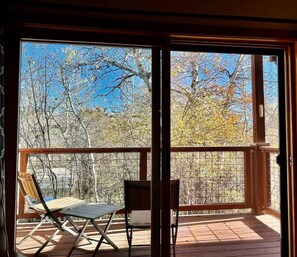 A wooden deck with two chairs and a table, overlooking a forested area. - Quiet condo near Targhee, Yellowstone, and Tetons. (Driggs)