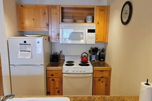A compact kitchen with a refrigerator, microwave, stove, and wooden cabinets. - Quiet condo near Targhee, Yellowstone, and Tetons. (Driggs)