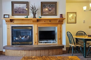 A living room with a fireplace, a television, and a dining area with chairs. - Quiet condo near Targhee, Yellowstone, and Tetons. (Driggs)