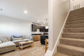 A modern living room with a sofa, coffee table, and a staircase leading to a kitchen area. - Teton Hideout - Sauna, AC, Garage (Driggs)
