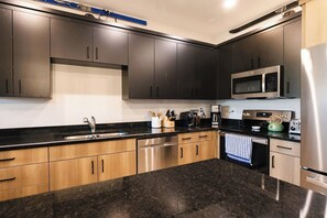 A modern kitchen with dark cabinets, stainless steel appliances, and a granite countertop. - Teton Hideout - Sauna, AC, Garage (Driggs)