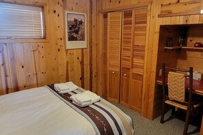 Ein Zimmer mit Holzboden, einem Bett, einem Sessel, einem Kleiderschrank und einem Bild an der Wand.