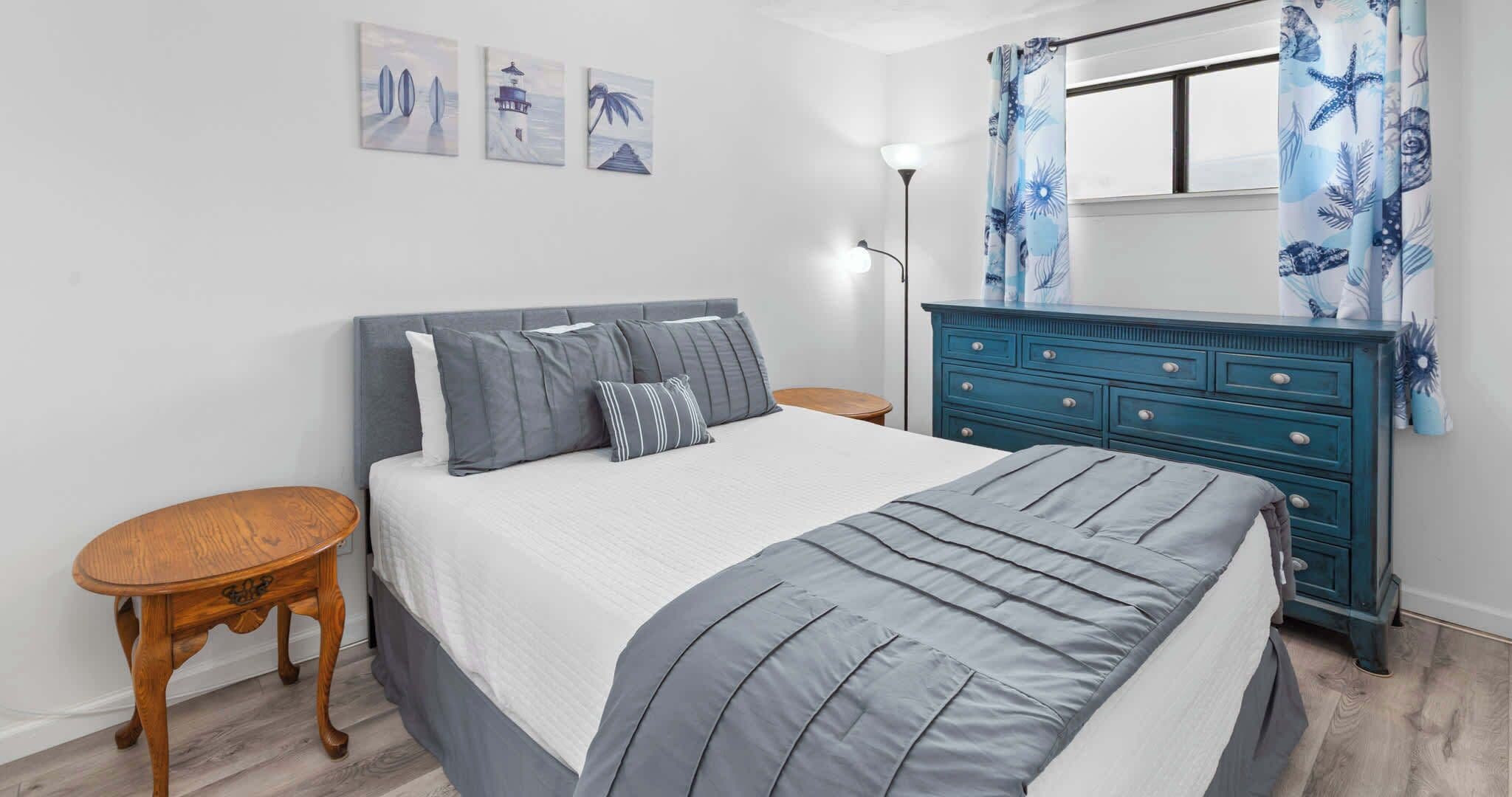 Quarto com cama, mesas de cabeceira, cômoda e obras de arte na parede.