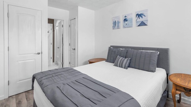 A bedroom with a bed, two bedside tables, and a door leading to another room. - PCB Beach Home With Gulf Access, Pool, and More (Panama City Beach)