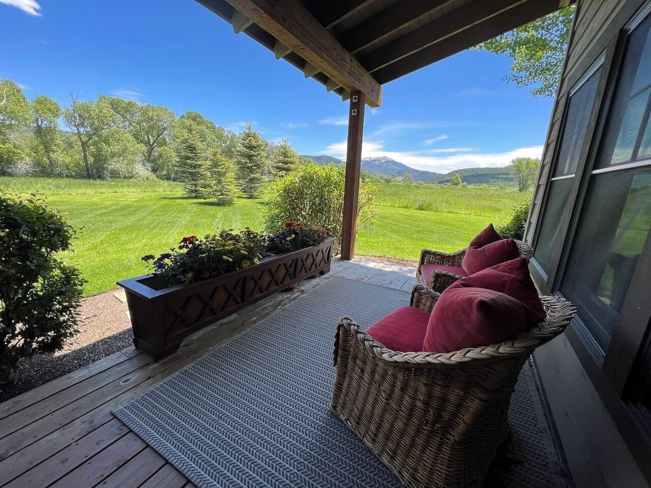 A covered outdoor seating area with wicker furniture and a view of a green landscape.