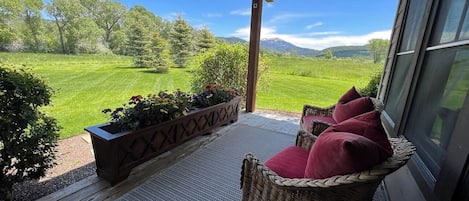 A covered outdoor seating area with wicker furniture and a view of a green landscape.