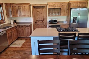 A kitchen with wooden cabinets, a microwave, a refrigerator, and a central island with chairs. - Trail Creek Retreat on Timberline (Victor)