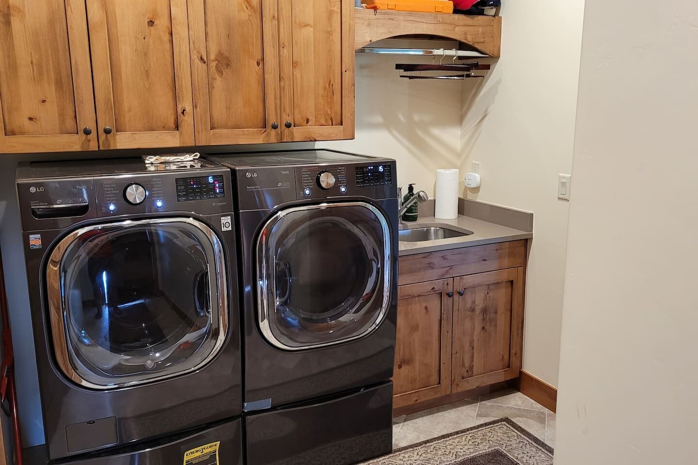 A laundry area with two front-loading washing machines, a wooden cabinet above, and a sink with a towel dispenser.