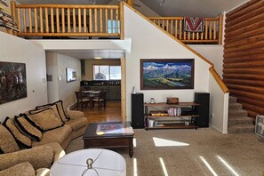 A spacious living room with a high ceiling, a dining area, a kitchen, and a staircase leading to an upper level. - Grizzly Home on Ski Hill Road, Targhee shuttle (Driggs)