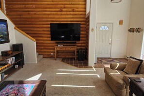 A log cabin interior with a television, wooden furniture, and a staircase. - Grizzly Home on Ski Hill Road, Targhee shuttle (Driggs)