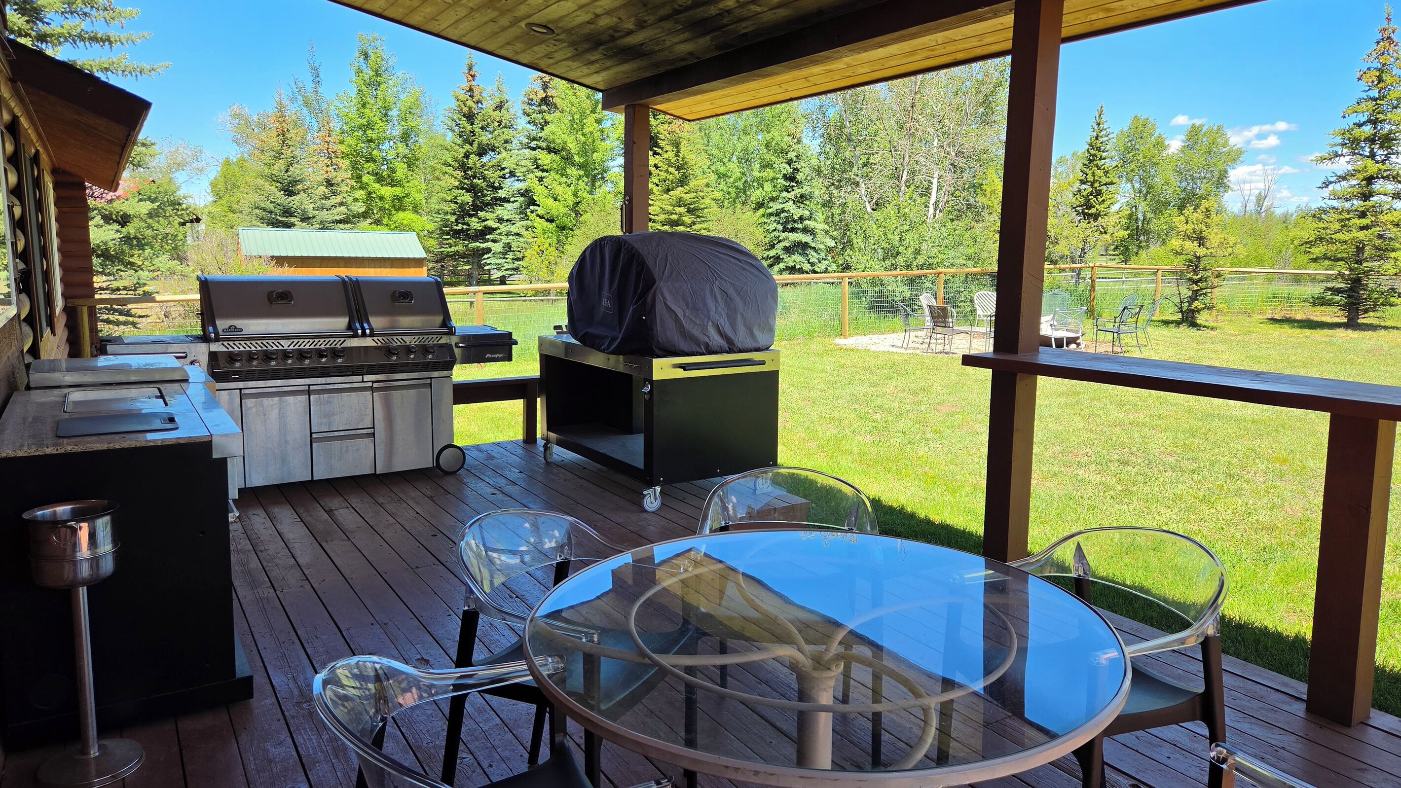 An outdoor deck with a grill, a table with chairs, and a view of a forest.
