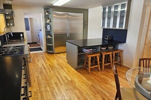 Una cuina moderna amb una illa central, tamboretes de fusta, fogó encastrat i nevera.