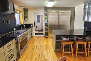 A modern kitchen with stainless steel appliances, wooden flooring, and bar stools. - Grizzly Home on Ski Hill Road, Targhee shuttle (Driggs)