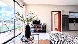 A modern living room with a large window, a black vase with white flowers, a television, and a patterned sofa. - Walking 2 Beaches, Dining, Shop, Fun, Nightlife (Punta Cana)