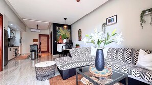 A modern living room with a patterned sofa, a glass coffee table, and a dining area with a mural. - Walking 2 Beaches, Dining, Shop, Fun, Nightlife (Punta Cana)