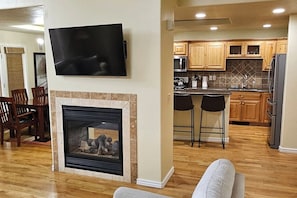 A modern living room with a fireplace, a flat-screen TV mounted above it, and a dining area with wooden chairs. - Mountain Town Getaway on Teton Creek (Driggs)