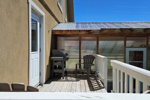 Ein überdachter Außenbereich mit Grill, Stühlen und Blick auf den Garten.