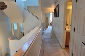 Ein Flur mit einer Holztreppe, einem Teppichboden und einer zur Toilette führenden Tür.