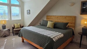 A bedroom with a sloped ceiling, a bed with a wooden headboard, two bedside lamps, a chair, and a window with blinds. - Sleeps 10! Updated Townhome Off Ski Hill Rd (Driggs)