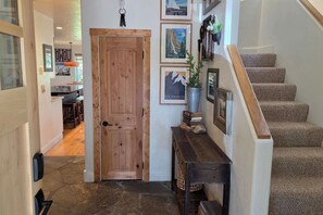 A hallway with a wooden door, a staircase, and a console table with framed pictures and a potted plant. - Sleeps 10! Updated Townhome Off Ski Hill Rd (Driggs)