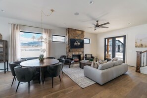 A spacious living room with a fireplace, a dining area with a round table, and a large window offering a view of the outdoors. - White Pine Lodge in Teton Valley (Driggs)