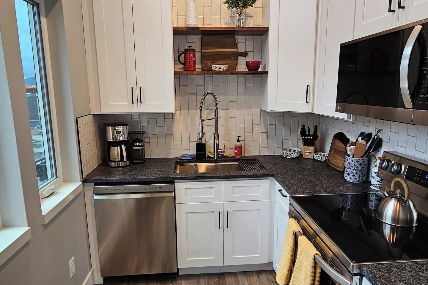 Una cocina moderna con armarios blancos, lavavajillas de acero inoxidable, encimera negra y microondas.