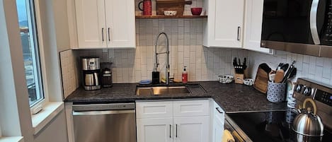 A modern kitchen with white cabinets, a stainless steel dishwasher, a black countertop, and a microwave.