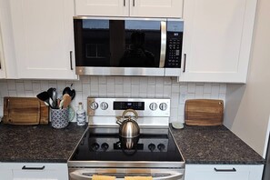 Een keuken met witte kastjes, een roestvrijstalen fornuis, een magnetron en een waterkoker.