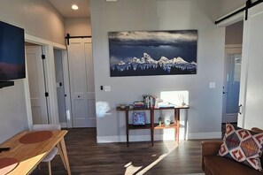 A modern living room with a wooden floor, a brown leather sofa, a coffee table, and a bookshelf with books and decorative items. - Table Rock Condo with huge south deck and a view. (Victor)