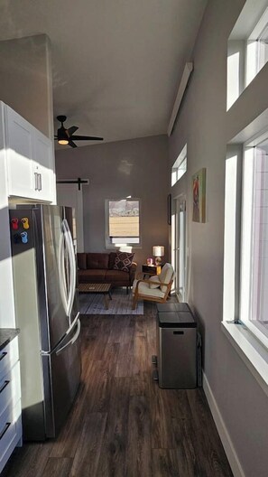 A compact kitchen with a refrigerator, a microwave, and a small trash bin. There is a window on the right side and a ceiling fan. - Table Rock Condo with huge south deck and a view. (Victor)