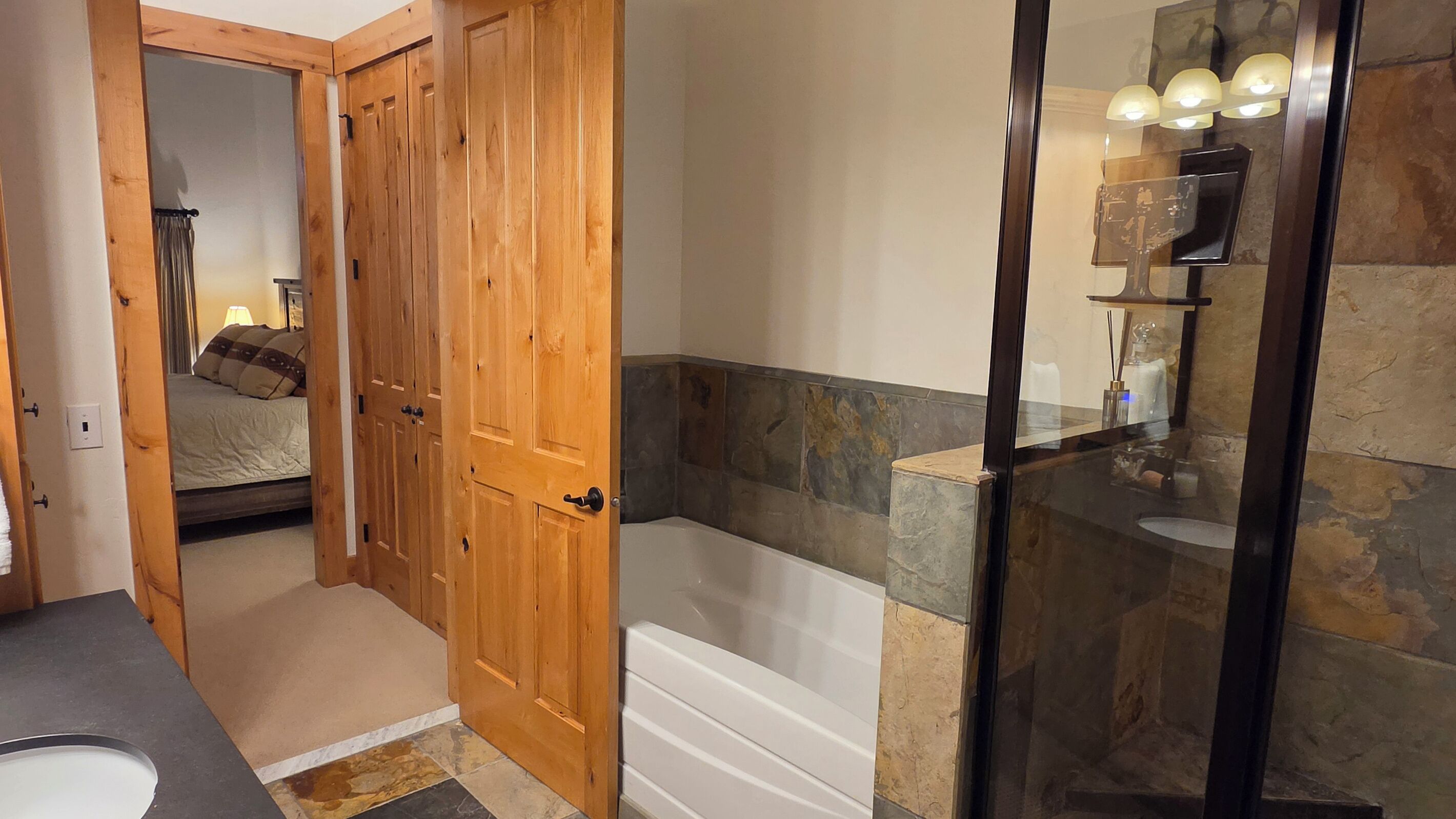 Un bagno con una vasca, una doccia e una porta in legno che dà su una camera da letto.