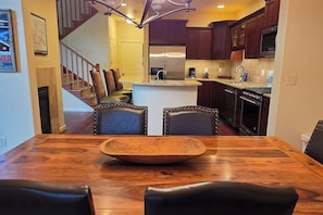 A dining area with a wooden table and chairs, a kitchen in the background, and a staircase leading to another level. - Teton Creek Getaway with Hot Tub (Driggs)