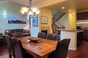 A dining area with a wooden table and chairs, a chandelier, and a kitchen with a refrigerator and a sink. - Teton Creek Getaway with Hot Tub (Driggs)