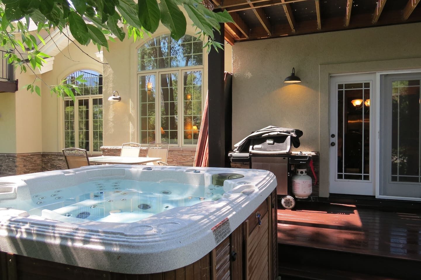 Een bubbelbad in een terras met een overdekte zithoek en een barbecue.