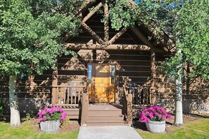 A wooden cabin with a porch, a wooden door, and potted plants. - It's Always "Peak" Season in the Tetons (Tetonia)