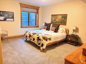 A bedroom with a bed, a window, a painting, and a nightstand. - It's Always "Peak" Season in the Tetons (Tetonia)