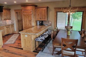A kitchen with wooden cabinets, a granite countertop, and a dining area with a table and chairs. - It's Always "Peak" Season in the Tetons (Tetonia)